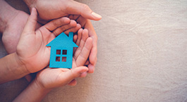 des mains qui protègent une petite maison